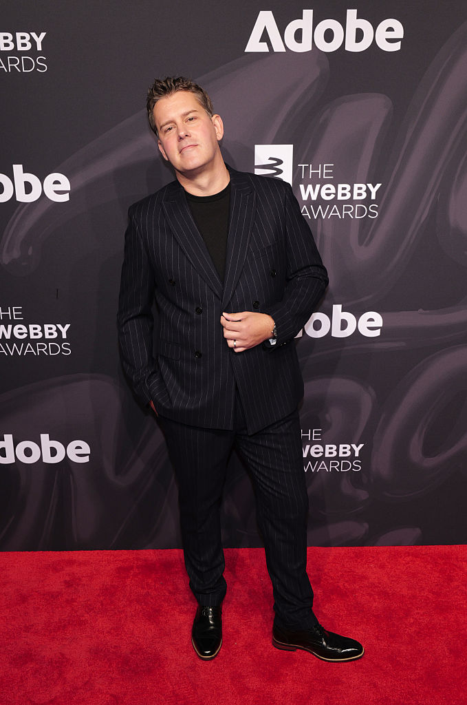 Dressed in a black pin-striped suit, Robert Newman, Managing Director at Carveco, stands on a red carpet with a backdrop featuring The Webby Awards' logo and Adobe's logo